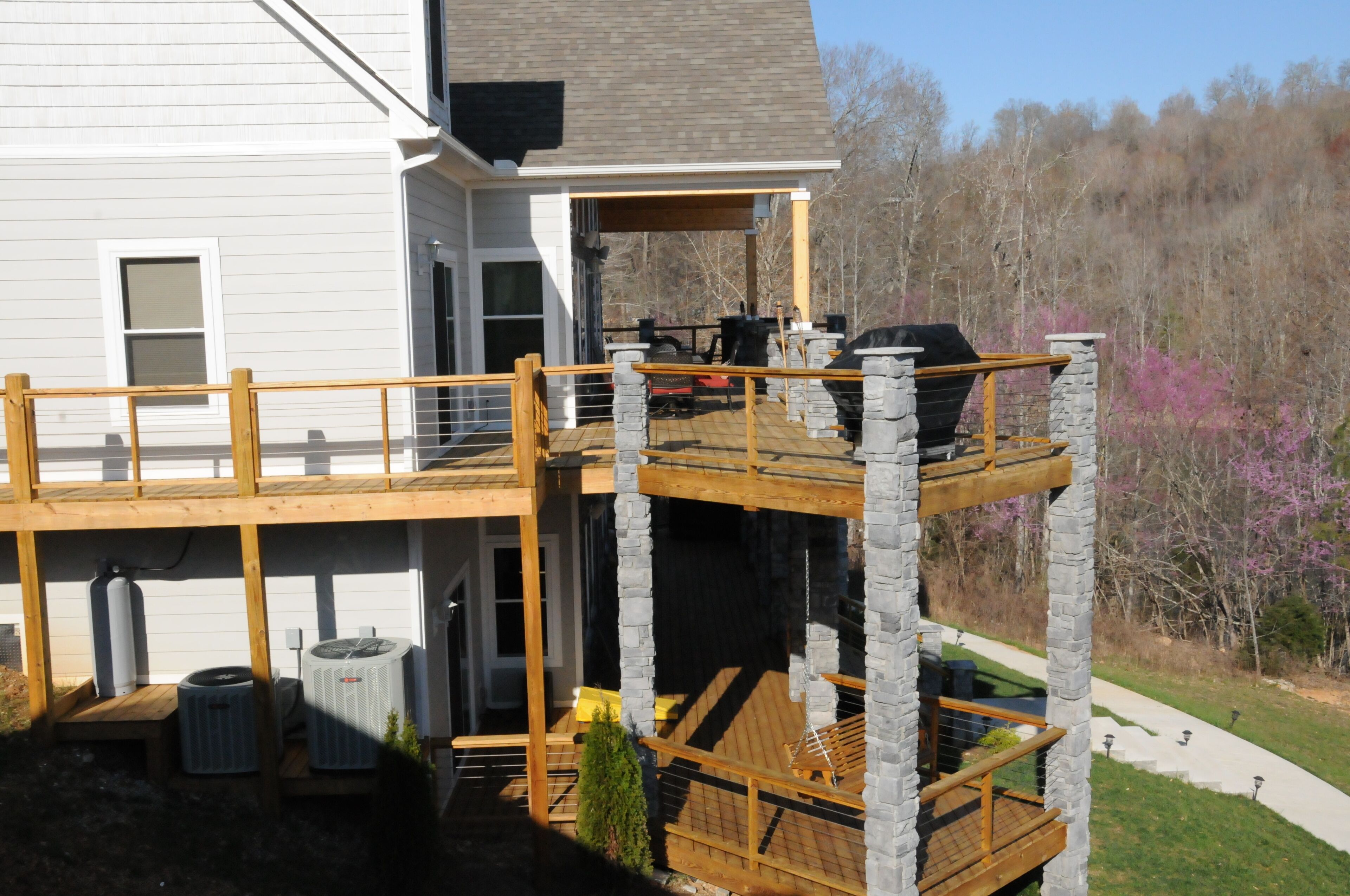 Une terrasse à deux niveaux, agrémentée de piliers en pierre, d’un espace salon extérieur et d’un coin barbecue.
