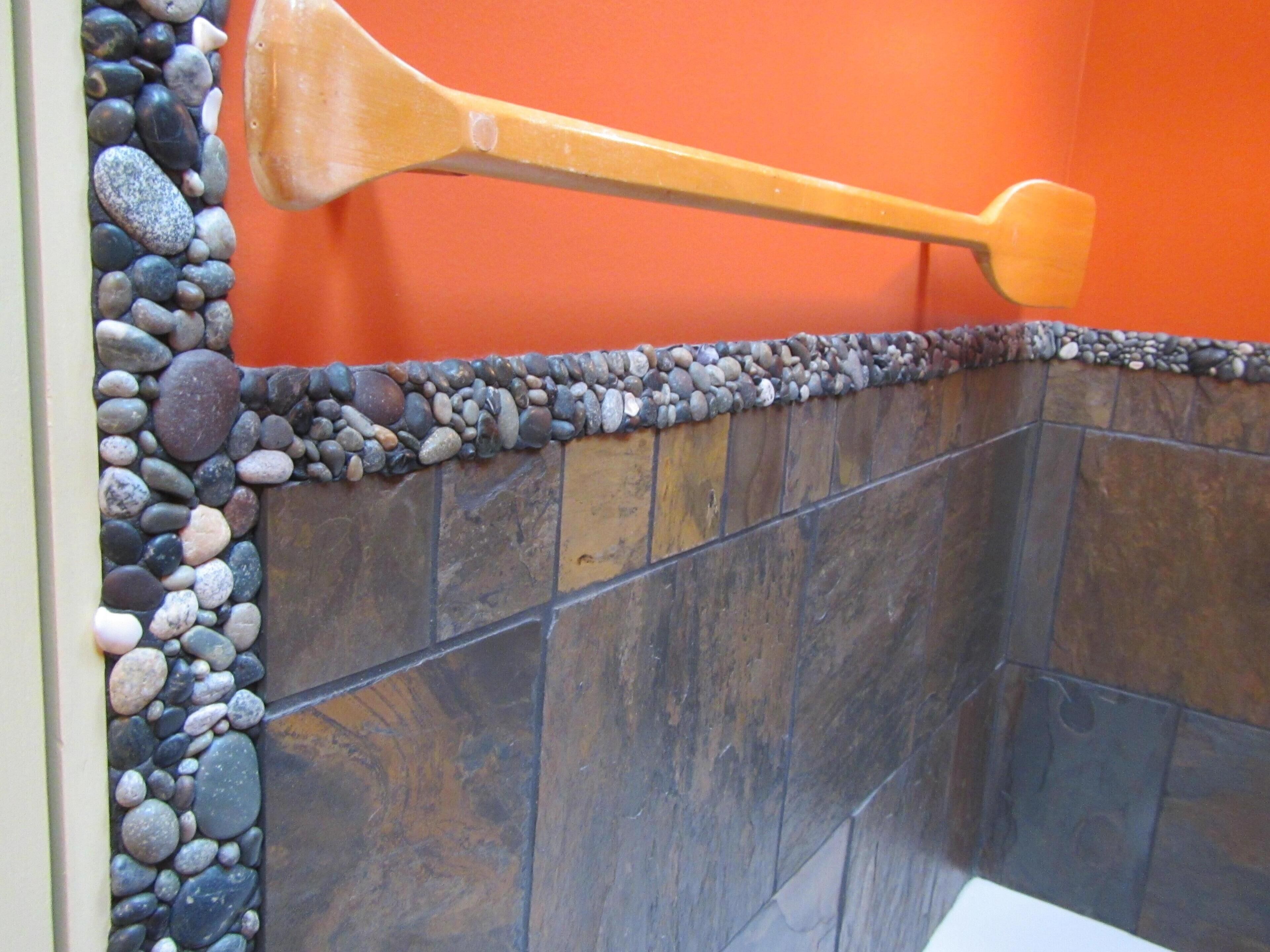 A corner of a bathroom with a stone wall, a wooden spatula, and a tiled floor.