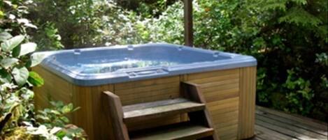 Ein Whirlpool auf einer Holzterrasse, umgeben von üppiger Vegetation.