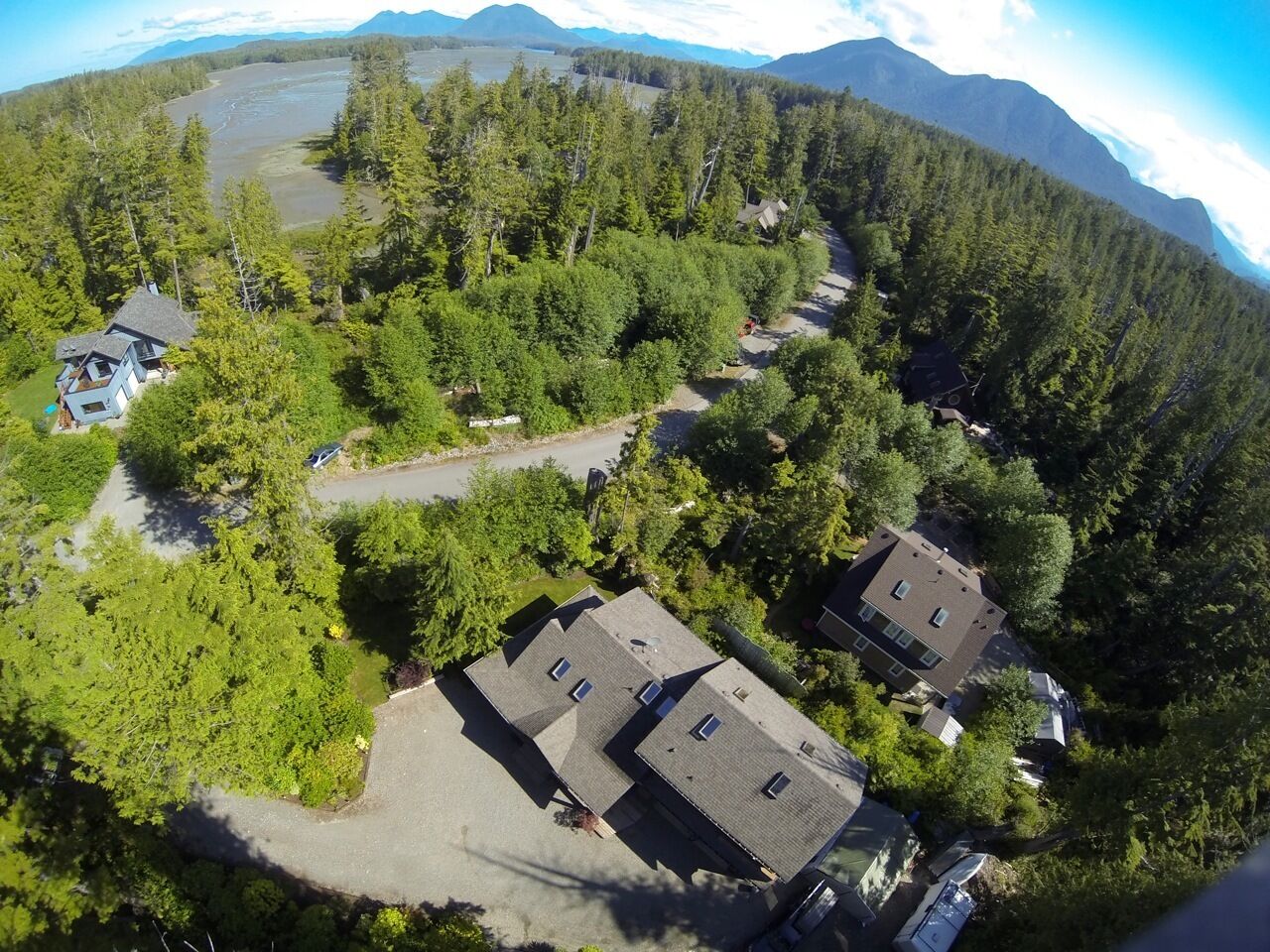 An aerial view of a residential area with two houses, surrounded by dense forest and a lake.