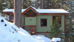 Une cabane à l’extérieur vert, avec des boiseries et un toit recouvert de neige.