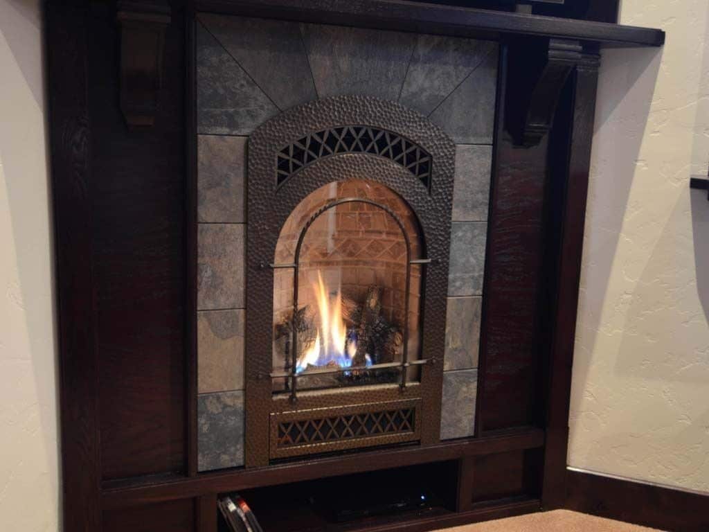 Une cheminée en pierre avec un feu qui crépite à l’intérieur, encadrée d’un bois sombre.