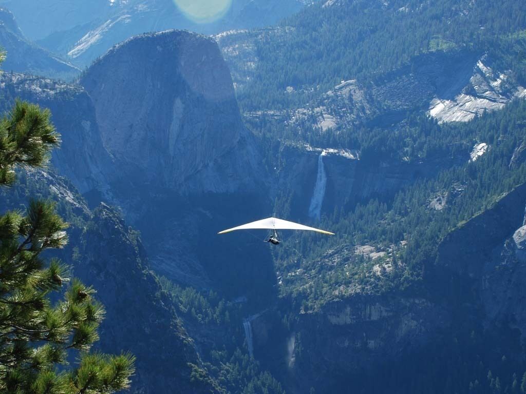 Een paraglider vliegt boven een bergachtig landschap met een waterval.