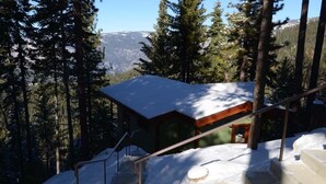 Une cabane dont le toit est recouvert de neige, entourée d’arbres et de montagnes.