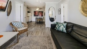 Ein modernes Wohnzimmer mit einer schwarzen Ledersofa, einem Korbstuhl mit gemusterten Kissen und einem Essbereich mit Tisch und Stühlen.