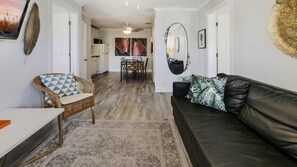 Un soggiorno moderno con un divano in pelle nera, una poltrona in vimini con cuscini decorati, e un'area pranzo con tavolo e sedie.