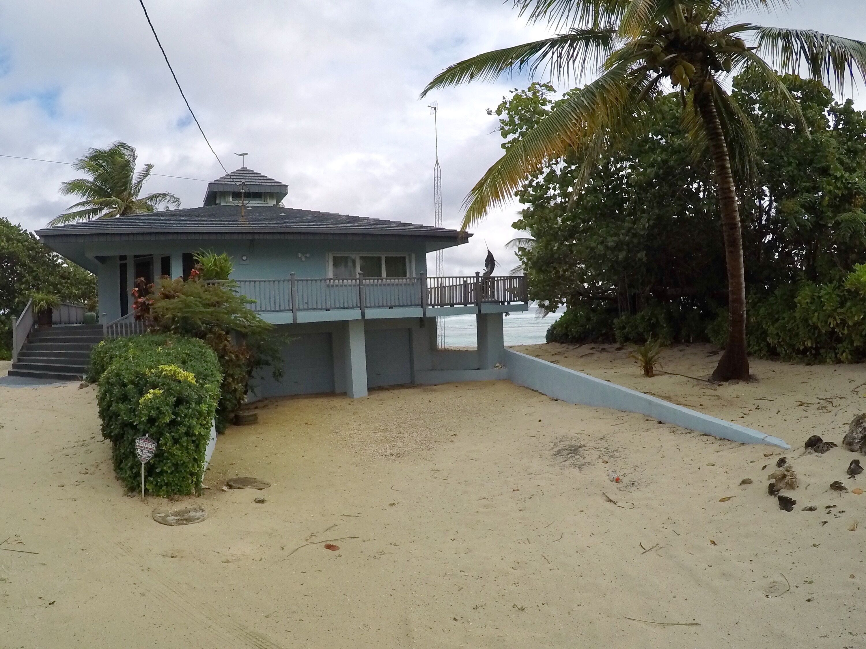 A beachfront property with a covered patio, a staircase leading to a balcony, and a sandy beach area.