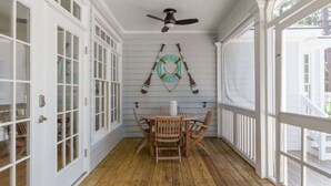 A covered porch with a wooden table and chairs, a ceiling fan, and a wall-mounted paddleboard sign.