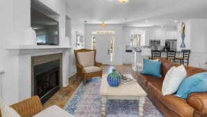 A spacious living room with a fireplace, a brown leather sofa, and a dining area in the background.