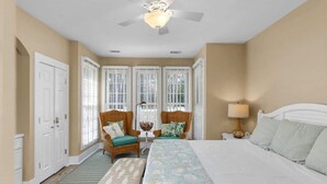 A bedroom with a bed, two chairs, a nightstand, a lamp, and a ceiling fan.