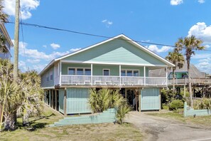 Ein zweistöckiges Haus mit Balkon, Veranda und kleinem Vorgarten mit Palmen.