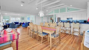 A spacious living area with a dining table, chairs, and a kitchen in the background. - Beach Front Folly Beach 6 Bedroom 7 Bathroom Sleeps 14 (Folly Beach)