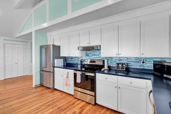 A modern kitchen with white cabinets, a stainless steel refrigerator, a black stove, and a blue countertop.