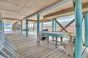 Ein überdachter Außenbereich mit Holzbänken und -tischen, einem Grill und Blick auf einen Zaun und Grünflächen.