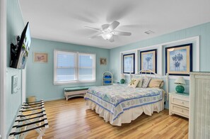 Ein Schlafzimmer mit einem Bett, einem Deckenventilator, einem Fenster mit Jalousien und einem Korbstuhl.