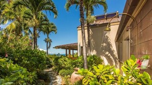 A tropical garden with a stone pathway, palm trees, and a pergola.