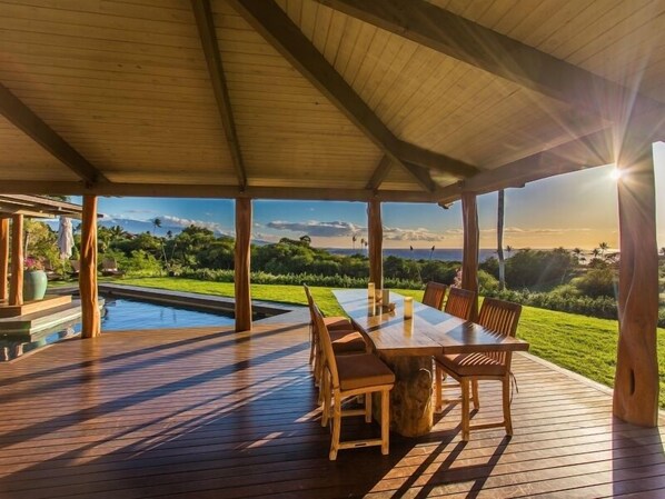 Un espacio cubierto para comer al aire libre, con piscina, terraza de madera y vistas del paisaje.