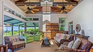 A spacious living area with a large window, green sofas, a coffee table, and a wooden ceiling.