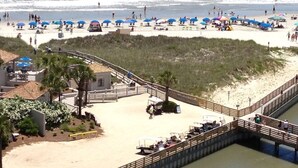 A beach with umbrellas, a wooden walkway, and a building with a patio. - Oceanfront Premium 3BR- Gourmet Kitchen! Farmhouse Decor! Gorgeous View! (Myrtle Beach)