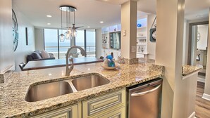 A modern kitchen with granite countertops, stainless steel appliances, and a dining area with a view. - Oceanfront Premium 3BR- Gourmet Kitchen! Farmhouse Decor! Gorgeous View! (Myrtle Beach)
