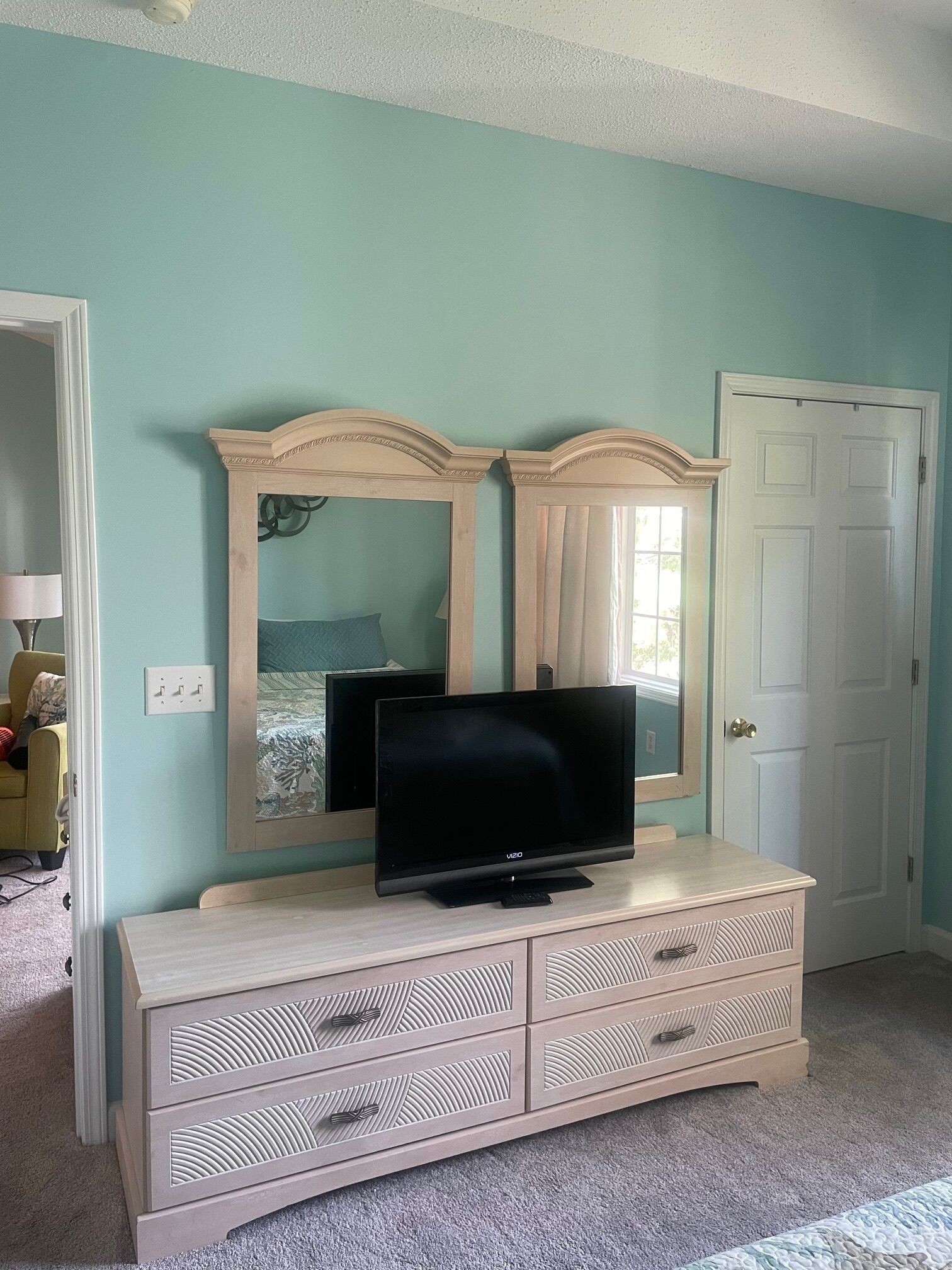 A bedroom with teal walls, a white door, a TV on a dresser, and a mirror above the dresser.