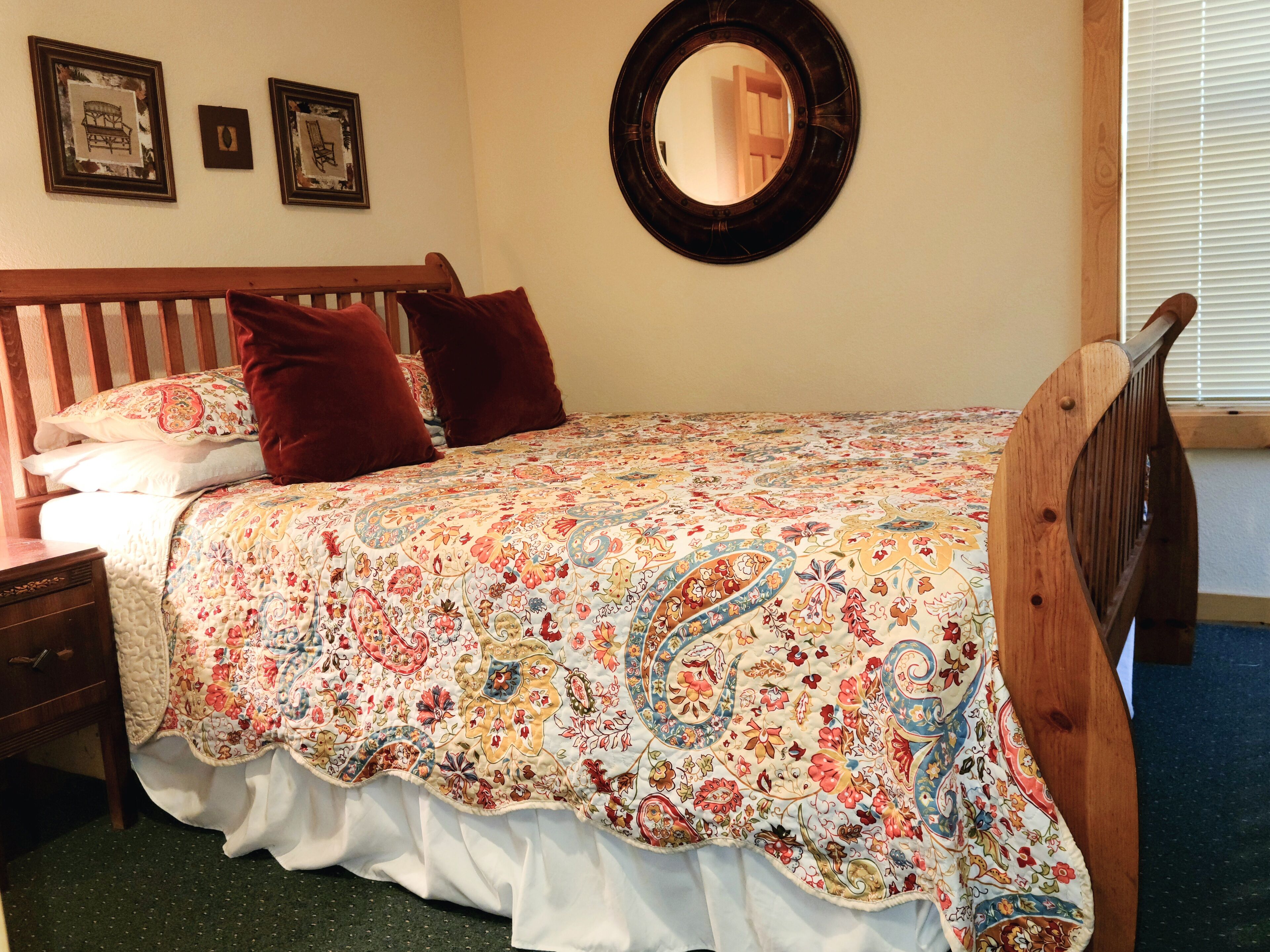 A bedroom with a wooden bed frame, a floral-patterned bedspread, a round mirror, and a nightstand.