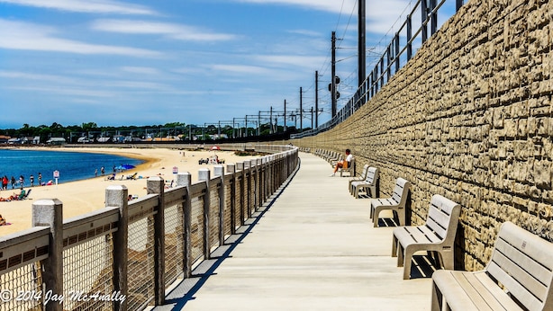 A concrete walkway with benches leading to a beach, overlooking the ocean.