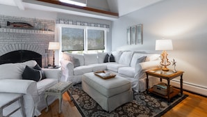 A modern living room with a white sectional sofa, a fireplace, and a large window with blinds.