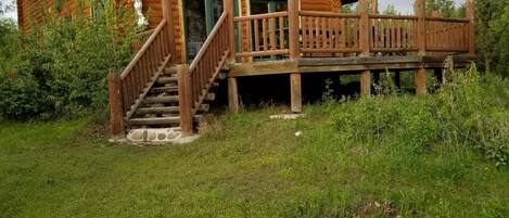 A wooden cabin with a green roof, a wooden deck, and a staircase leading to the entrance.