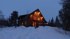 A log cabin with a prominent chimney, surrounded by snow and trees. - Secluded Lakefront Log Cabin, Wildlife and Fishing Paradise, Pet Friendly (Ashton)