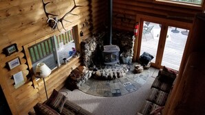 A cozy cabin interior with a stone fireplace, wooden walls, and a view of the outdoors. - Secluded Lakefront Log Cabin, Wildlife and Fishing Paradise, Pet Friendly (Ashton)