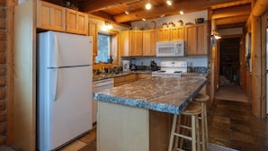 A kitchen with wooden cabinets, a granite countertop, a refrigerator, a microwave, and a stove. - Secluded Lakefront Log Cabin, Wildlife and Fishing Paradise, Pet Friendly (Ashton)