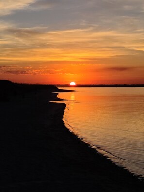 A sunset over a calm body of water with a silhouette of a beach and a distant shoreline.
