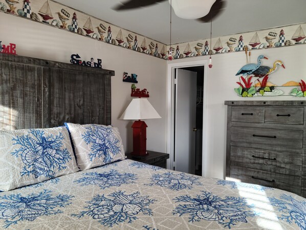 A bedroom with a bed, a nightstand, a dresser, and a door leading to another room.