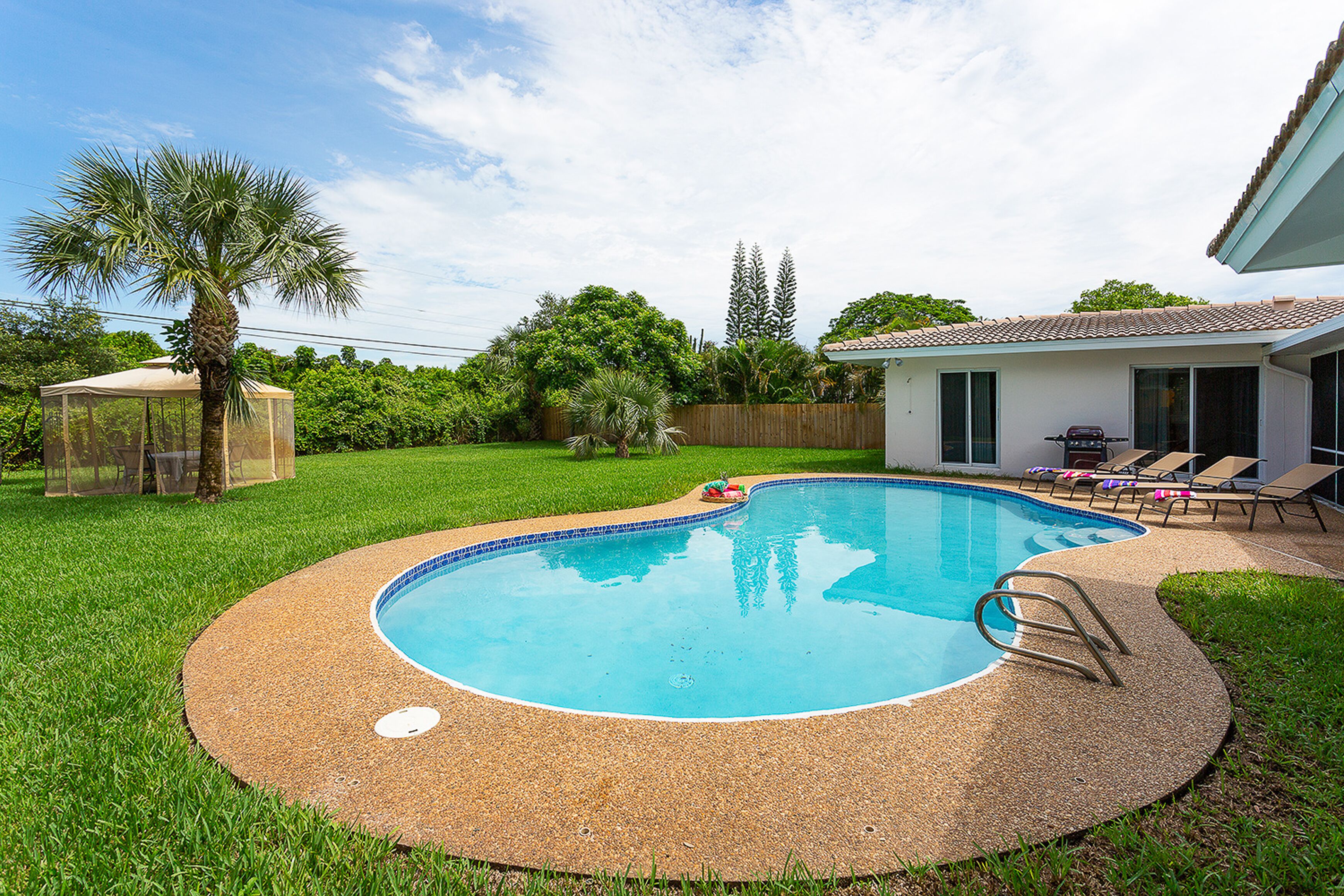 A backyard with a swimming pool, a covered play area, and a patio with lounge chairs.