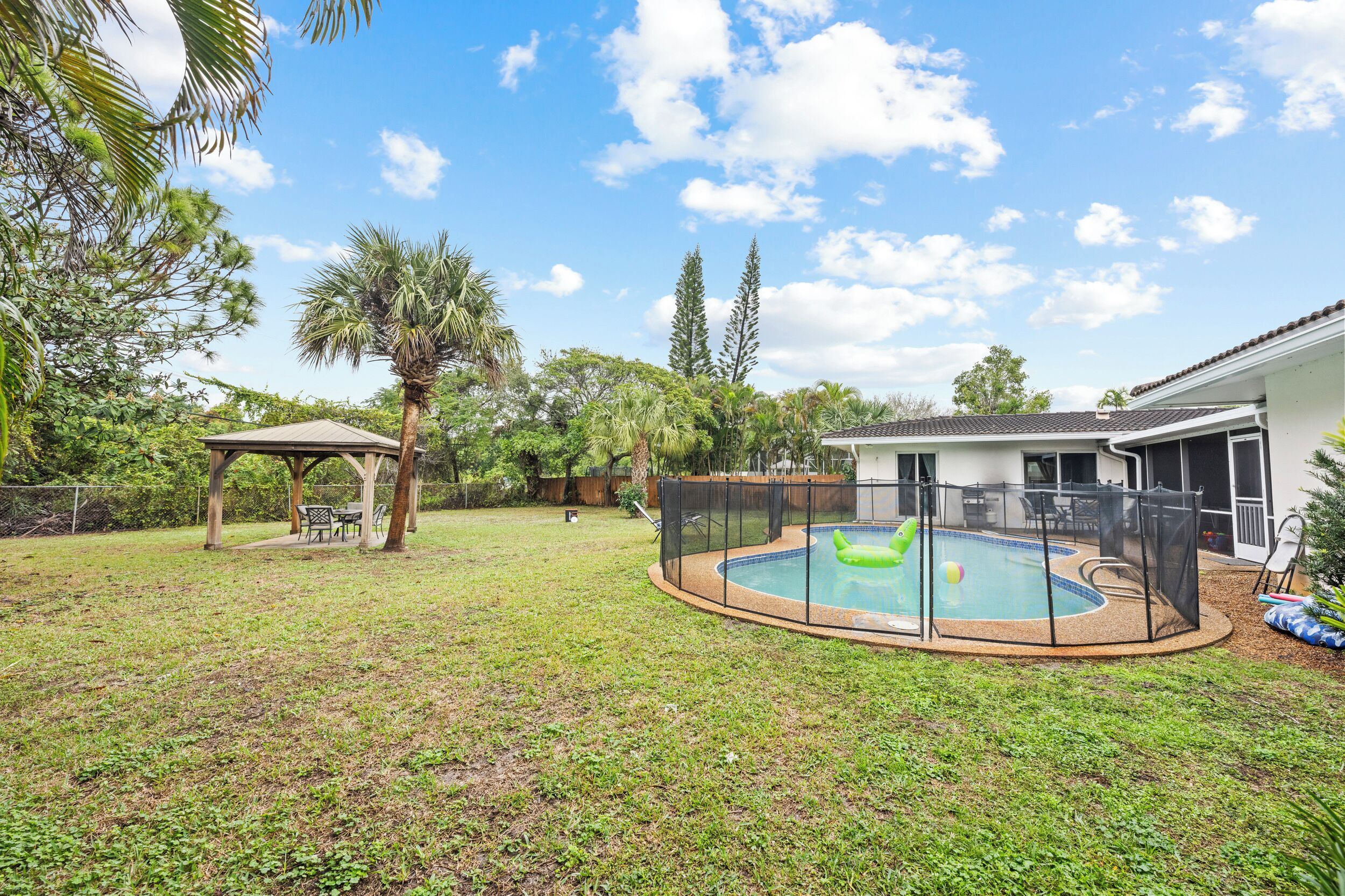 A backyard with a swimming pool, a covered patio, and a fenced area.