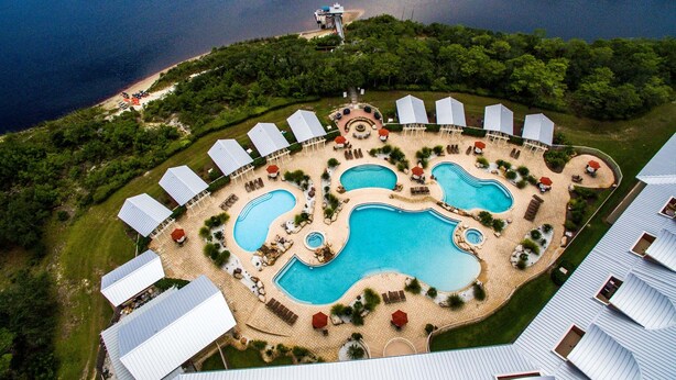 Vista aérea de un resort con varias piscinas, zonas de descanso y un muelle junto al agua.