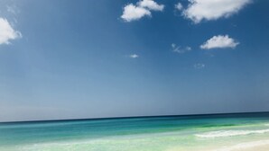 Una playa con agua turquesa cristalina y una orilla arenosa bajo un cielo azul con nubes dispersas.
