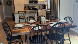 A modern kitchen with white cabinets, a stainless steel refrigerator, and a dining area with a wooden table and black chairs. - "Moss Mountain Cottage" Clean, Private, Central MDI - 2025 updated kitchen (Bar Harbor)