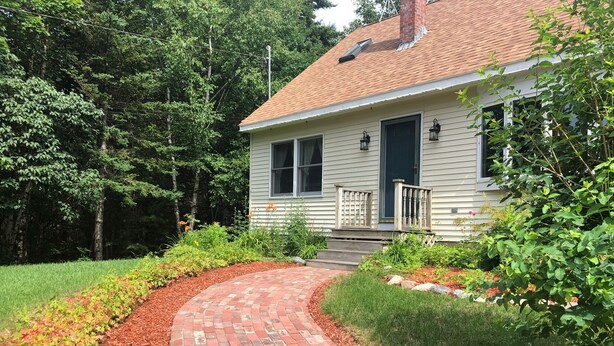 A house with a brick pathway leading to the front door, surrounded by a garden with various plants and a lawn. - "Moss Mountain Cottage" Clean, Private, Central MDI - 2025 updated kitchen (Bar Harbor)