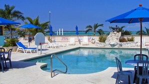 A pool area with lounge chairs and umbrellas, a stone wall, and a view of the ocean.