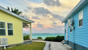 A pathway leading to a yellow and a blue house with a view of the ocean.