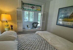 Un dormitorio con dos camas, una ventana con persianas, una lámpara, una silla y un cuadro enmarcado.
