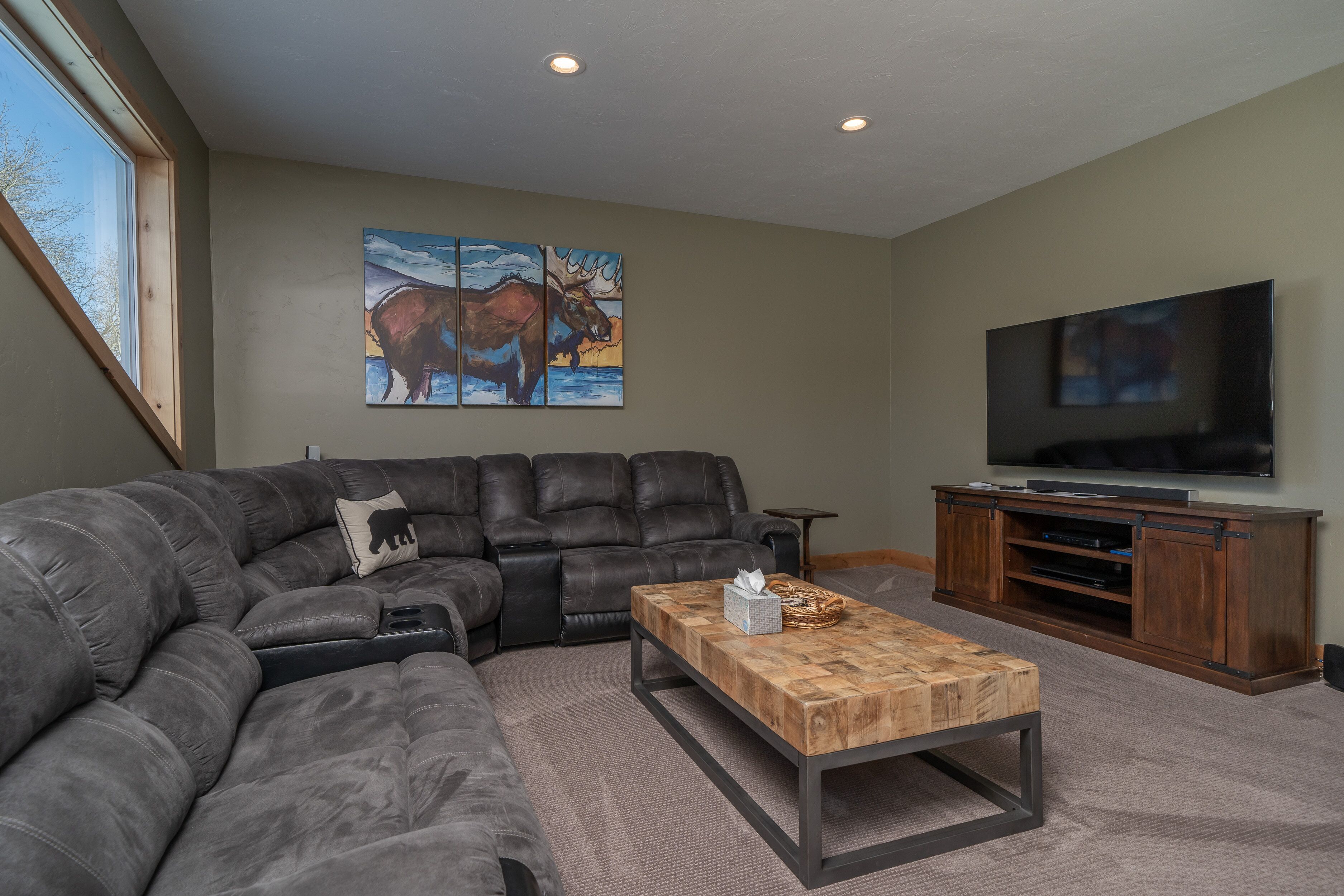 A modern living room with a sectional sofa, a wooden coffee table, a flat-screen TV, and a painting of horses on the wall.