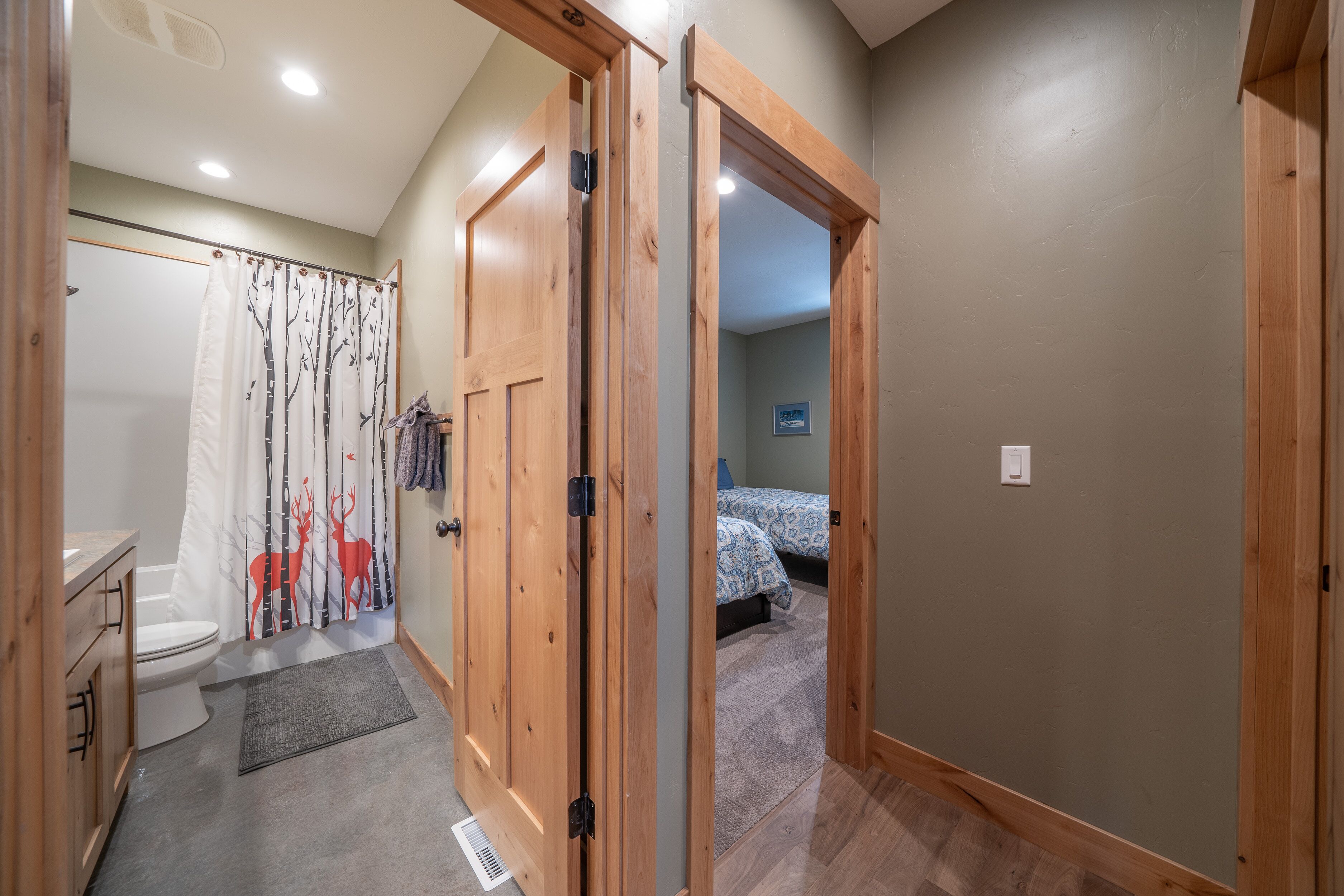 A hallway leading to a bedroom with a bed, a bathroom with a toilet and shower curtain, and wooden doors.