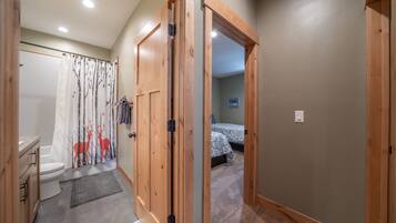 A hallway leading to a bedroom with a bed, a bathroom with a toilet and shower curtain, and wooden doors.