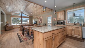 Una cocina amplia con armarios de madera, encimeras de granito y una isla grande. Hay un comedor con mesa y sillas, y una sala de estar con sofá y chimenea.