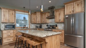 Una cocina con armarios de madera, un refrigerador de acero inoxidable, una encimera de granito y taburetes de bar.