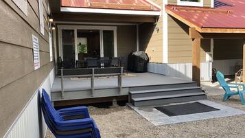 A covered outdoor area with a patio, steps leading up to a deck, and a grill.