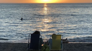 Deux chaises de plage sont placées face à l’océan, avec un coucher de soleil en arrière-plan.